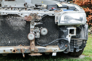 Wall Mural - A detail of the old car wreck. The front of the car is visible, some parts are missing. The engine and radiator are without cover. 