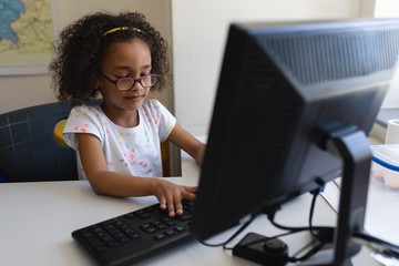 Front view little schoolgirl using desktop pc at desk in