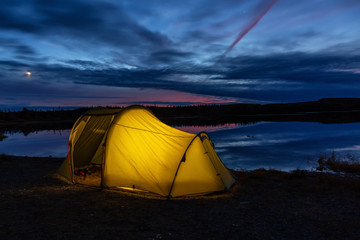lit tent in nature near a calm lake during a vibrant sunset. taken in northern newfoundland, canada.