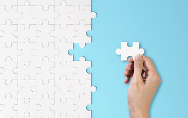 Hand putting a piece of white jigsaw puzzle. Pattern texture separated in strategy and solution of team business success partnership concept on blue background.