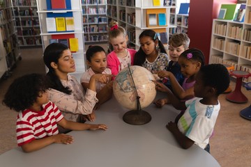 Wall Mural - Female teacher teaching the kids about the globe at table in