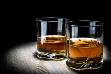 Two glasses of whiskey on a vintage wooden table on a black background.