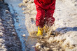 Kid legs in rainboots jumping in the ice puddle