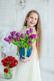 Fototapeta Tulipany - Portrait of a beautiful blue-eyed child, a little girl with a bouquet of tulips in a bright room.