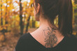 Tattoo on the back of a young girl with reddish hair dressed in a poncho in an autumnal forest