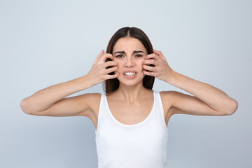 Young woman scratching face on light background. Annoying itch