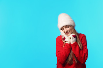 Canvas Print - Portrait of emotional young woman in stylish hat, sweater and mittens on color background, space for text. Winter atmosphere