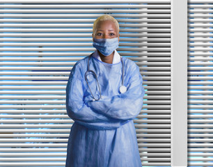 attractive and confident black African American medicine doctor wearing face mask and blue scrubs standing corporate isolated at hospital room with Venetian blinds