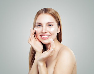 Beautiful model girl applying cosmetic cream treatment on her face on white. Healthy woman portrait