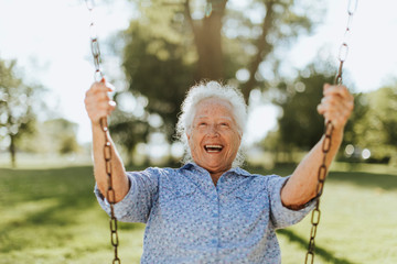 Cheerful senior woman on a swing at a playground