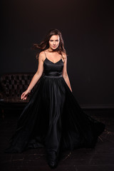 Wall Mural - Portrait of young woman in elegant silk black dress posing in a dark interior, fashion beauty photo