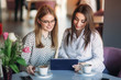 © Aleksandr - Two girls use a tablet while sitting in a cafe and drinking coffee. Business woman