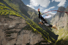 A Man In A Helmet Jumps Ropeup With An Empty Flag In The Mountains. Extreme Sports. Leisure