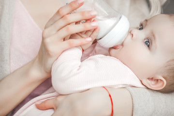 Wall Mural - Young mother feeding her little cute baby daughter with bottle of child formula. Woman with her newborn baby at home. Mom taking care of a child. Alternative to breast feeding.