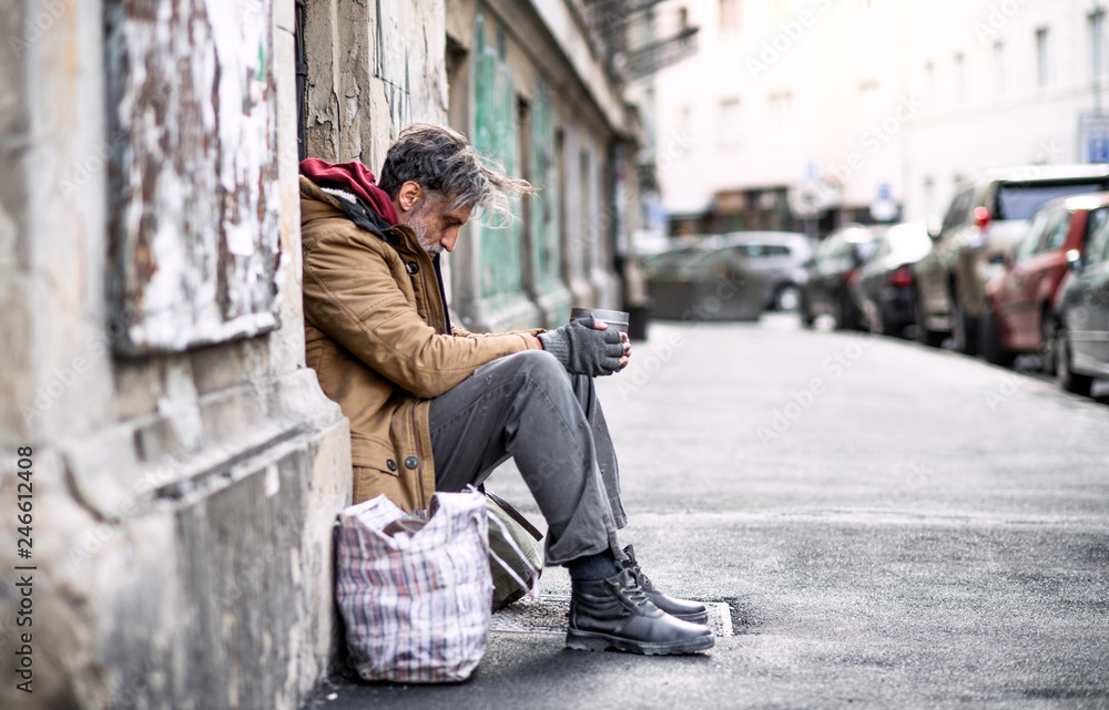 Homeless beggar man sitting outdoors in city asking for money donation. - obrazy, fototapety, plakaty 