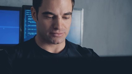 Portrait of developer programmer working on computer in a data center filled with monitor screens. Steadicam shot