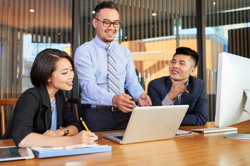 Smiling Asian businessman presenting his idea to coworkers at meeting