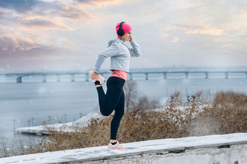 Young athlete stretching on a winter day near city background