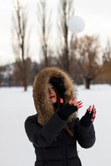 Wall Mural - Beautiful young woman with long nails, playing with snowball. Snow all around her. Park scene, blurred background.