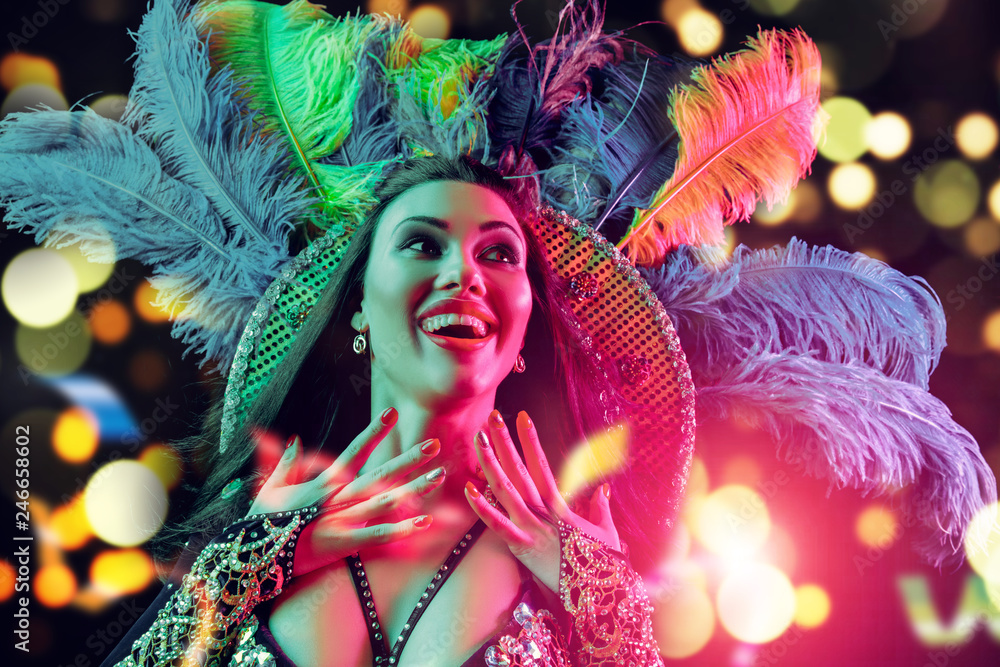 Beautiful young woman in carnival peacock costume. Beauty model woman at party over holiday background with magic glow. Christmas and New Year celebration. Glamour lady with perfect make up and