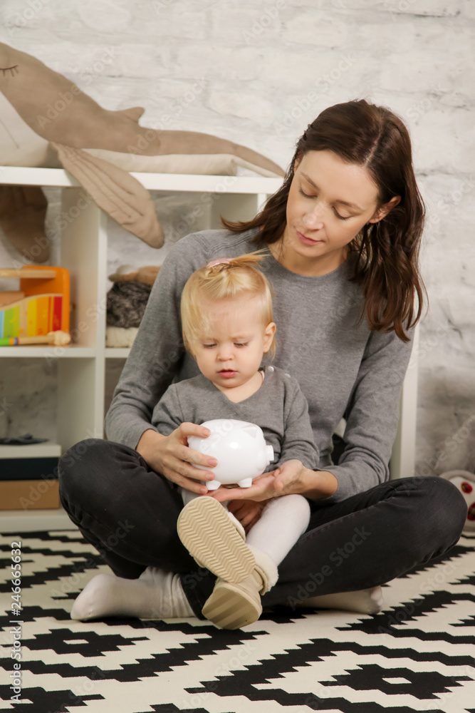 Mother and her baby girl putting a coin into a piggy bank. Mom teaches ...