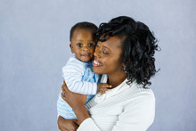 Beautiful African Amercian Woman WHolding Her Baby Boy On A Gray Background
