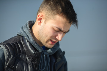 Portrait of an angry young handsome guy in a black vest on the street in spring.