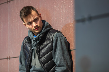 Portrait of an angry young handsome guy in a black vest on the street in spring.