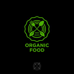 Organic food logo. Green food emblem. Green leaves, fork and spoon in a circle isolated on a dark background. Nature health meal, vegetarians emblem.