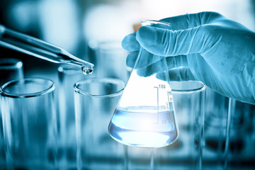 hand of scientist holding flask with lab glassware in chemical laboratory background, science labora