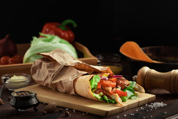 Wall Mural - Mexican burrito wrap with corn tortilla, chicken meat and vegetables on dark rustic background. Chicken grilled shawarma with bacon, pita bread, tomatos and salad and different sauces.