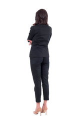 Wall Mural - Back view of business woman in black suit with crossed arms watching interested. Full body isolated on white background. 