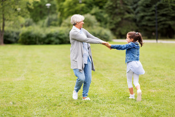 family, leisure and people concept - happy grandmother and granddaughter playing game or dancing at summer park