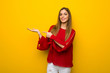© luismolinero - Young girl with red dress over yellow wall holding copyspace imaginary on the palm to insert an ad