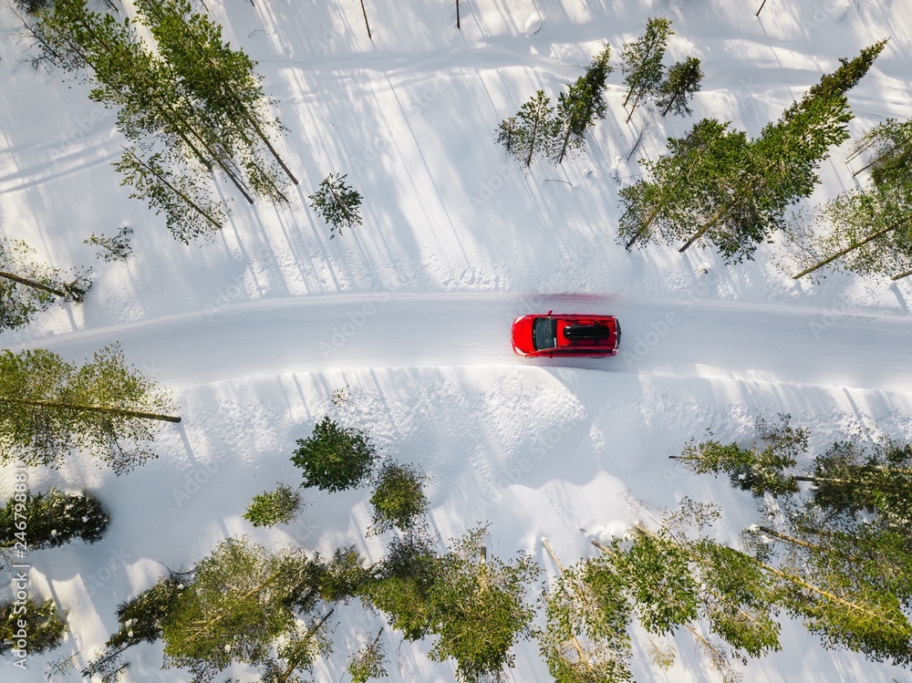 Aerial view of red car driving through the white snow winter forest on country road in Finland, Lapland. - obrazy, fototapety, plakaty 