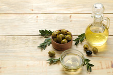 Green Olives With Leaves In A Wooden Bowl With Olive Oil On A Natural Wooden Table. Space For Text
