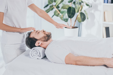 Wall Mural - cropped shot of reiki healer doing treatment session to calm bearded man with closed eyes