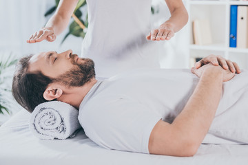 Wall Mural - cropped shot of bearded man with closed eyes receiving reiki treatment