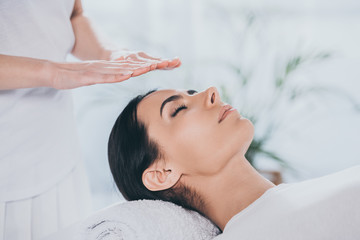 Wall Mural - close-up view of peaceful young woman with closed eyes receiving reiki treatment