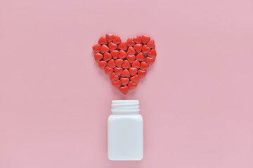 A heart shape of medicine pills pouring out of white bottle on pink background. Concept of Valentine's Day or pharmacy, Medical.