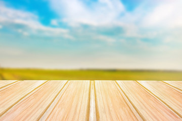 Wall Mural - Empty wooden table with blurred green field on background and blue sky