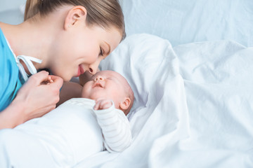 Wall Mural - smiling young mother holding hand of adorable newborn baby lying on bed