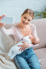 Wall Mural - high angle view of happy young woman breastfeeding baby and taking selfie with smartphone at home