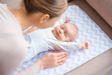 Wall Mural - high angle view of young mother looking at adorable infant baby lying on sofa