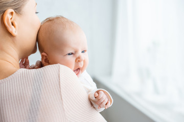 Wall Mural - cropped shot of young mother kissing adorable newborn baby at home