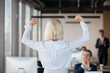 © fizkes - Rear view at middle aged businesswoman team leader raising hands celebrating business success concept, excited by goal achievement, new opportunities, company profit or growth in corporate office