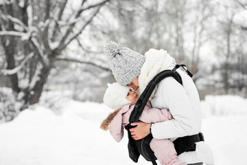 Little baby girl and her mother walking outside in winter Mother is holding her baby babywearing in the ergo carrier