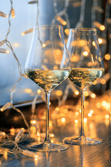 Closeup of two glasses of white wine in transparent crystal glasses on background of window and garlands. Concept romantic dinner in Michelin premium restaurant, party, February 14, March 8