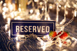 Closeup strawberry, two glasses champagne sparkling wine, reserved nameplate on wooden table, window, garlands, lights, bokeh. Concept date evening in restaraunt, 8 march, Valentine Day, christmas
