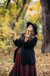 © sushytska - Beautiful autumn girl in the park. Lots of yellow leaves. Girl in a gray coat and red dress. Pregnant girl holding hands belly